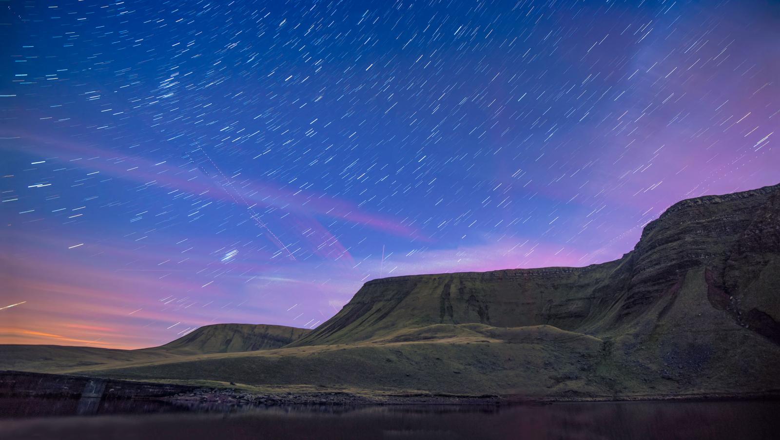 Llyn a mynydd yn erbyn awyr las tywyll a phorffor y nos, yn llawn sêr.