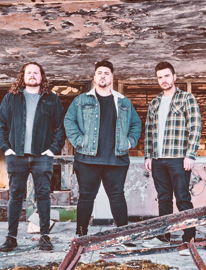 Five men stand in a line looking straight ahead with an industrial background