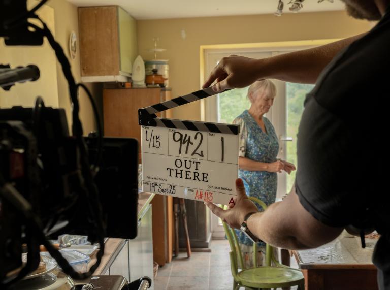 Clapper board raised in front of camera, shooting interior kitchen scene of female cast member
