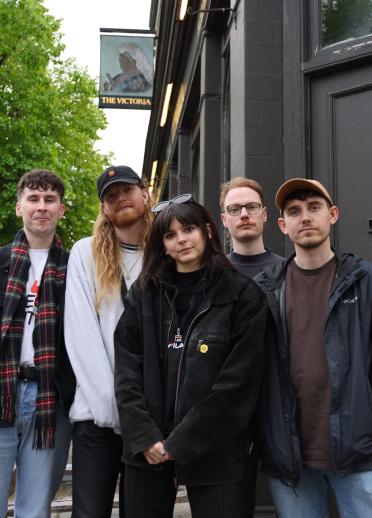 four male band members and one female stood outside a music venue/pub