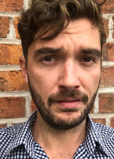 man with brown hair beard and moustached looks directly in to the lens.