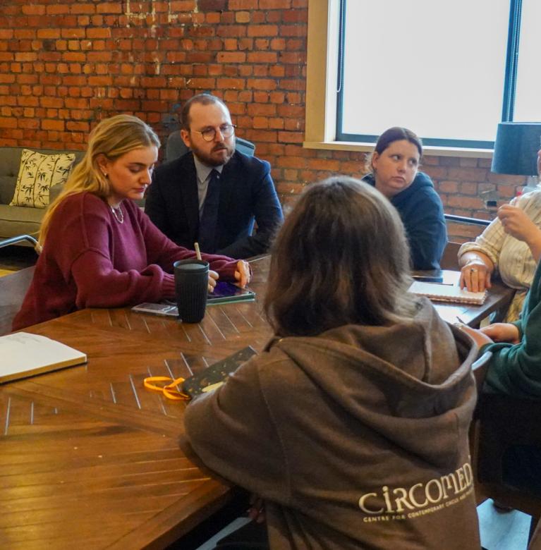 a group of 6 women and one man sit around a table on a training session