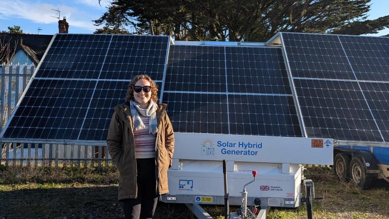 Person standing in front of a solar hybrid generator with solar panels and a tree in the background