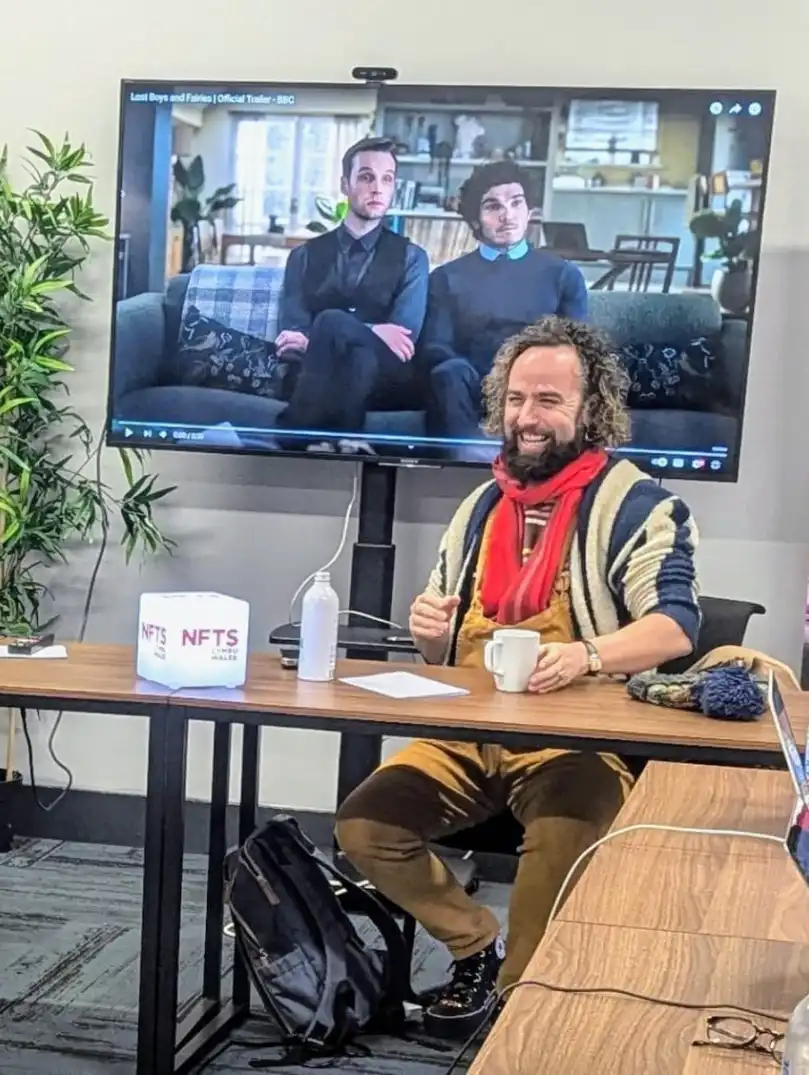 Workshop discussion at NFTS Cymru Wales with participants seated at a table, a presentation screen, and promotional banner in view