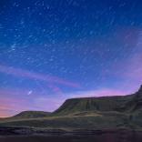 Llyn a mynydd yn erbyn awyr las tywyll a phorffor y nos, yn llawn sêr.