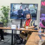 Workshop discussion at NFTS Cymru Wales with participants seated at a table, a presentation screen, and promotional banner in view